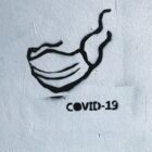 a black graffiti outline of a mask sketched onto a white background with the word covid-19 below