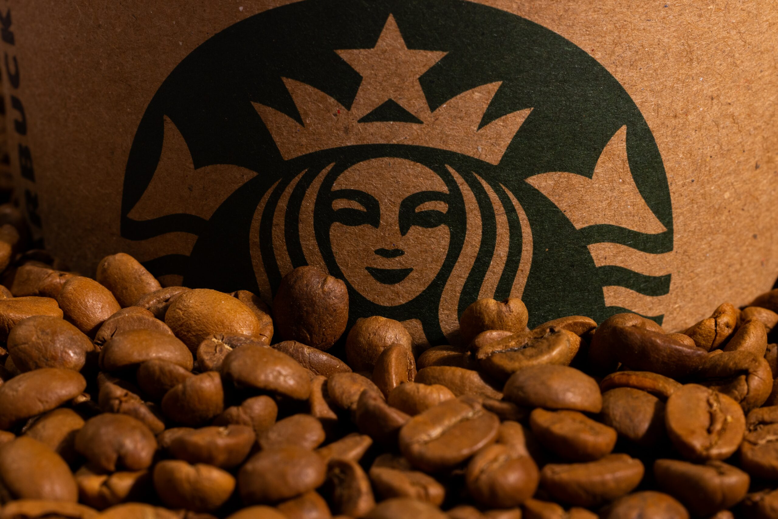 a close up of the starbucks green siren logo on a cardboard background in front of a pile of coffee beans