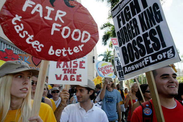 on the ground view of protestors holding signs that read "fair food tastes better" and "fight burger king bosses" and "raise the wage"