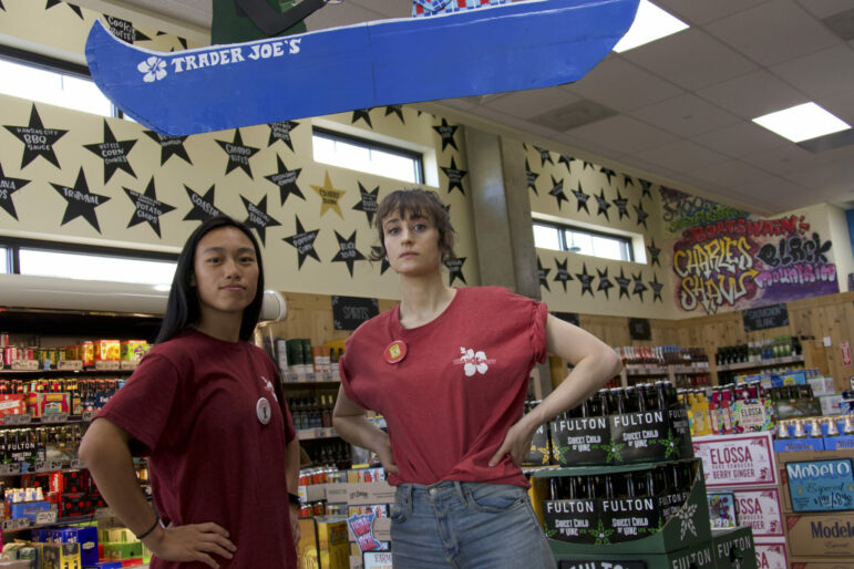 one asian and one white woman stand powerfully in trader joe's grocery store, stars like the walls behind them